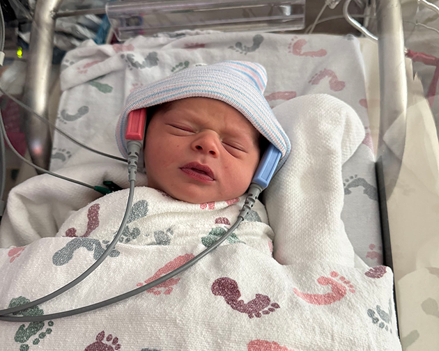 Newborn asleep in a nursery bassinet while hearing is being screened using automatic auditory brainstem response (AABR) technology.